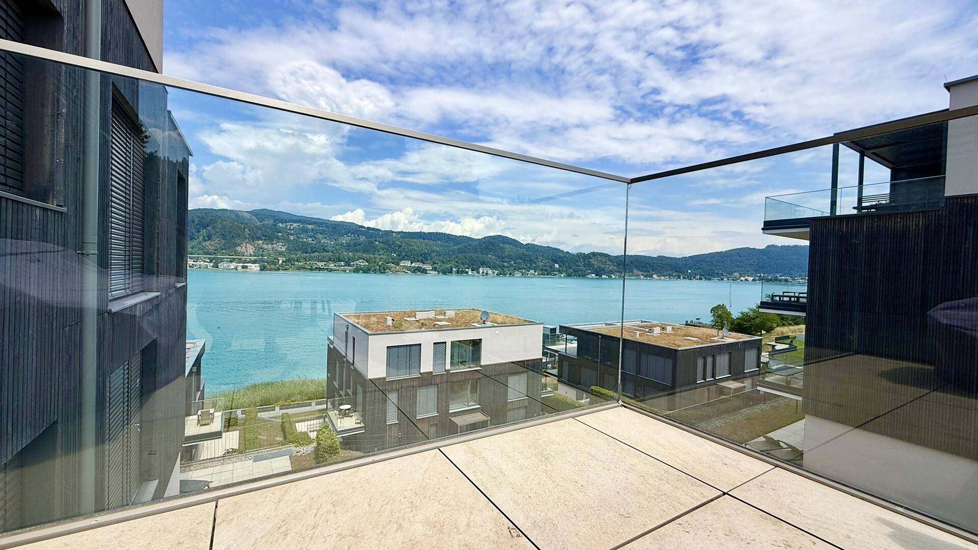 Eckterrasse mit Glasgeländer bietet einen weiten Blick über den See und die Bergkette.