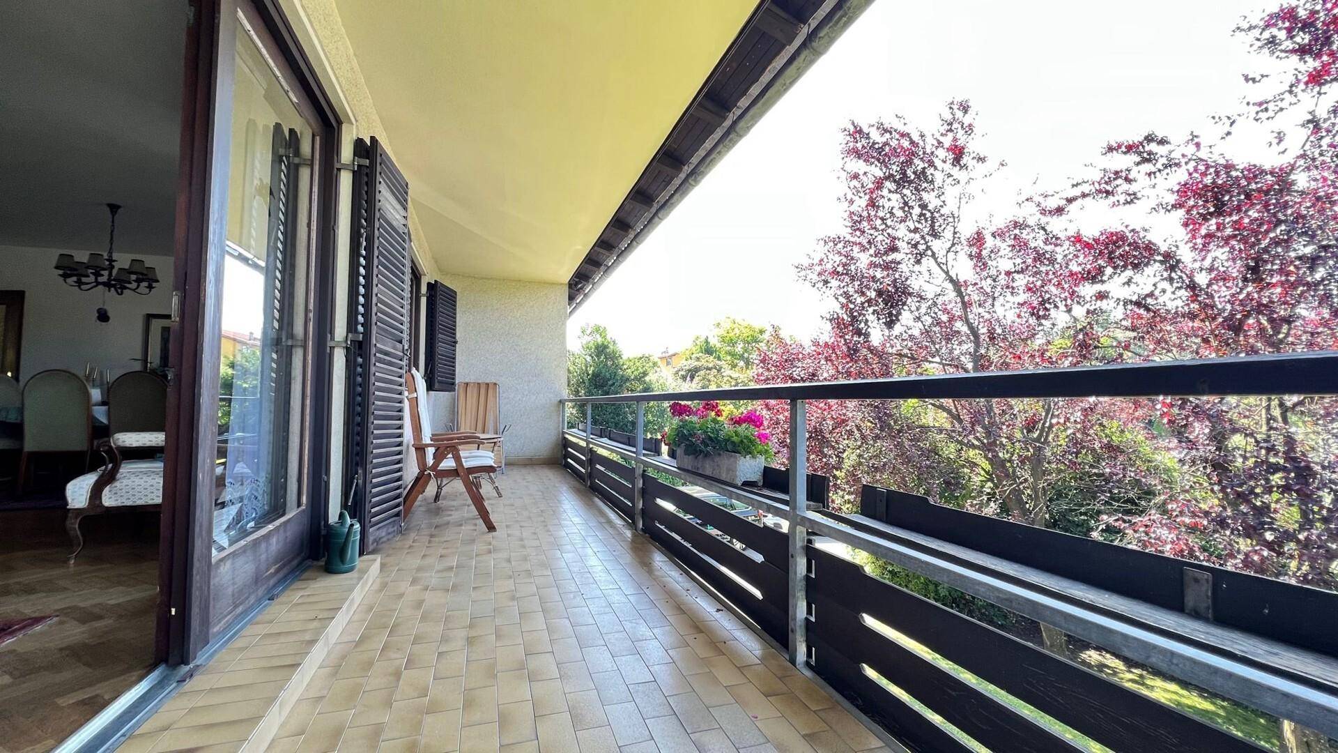 Heller Balkon mit Fliesenboden und Zugang vom Innenbereich, umgeben von Grün.