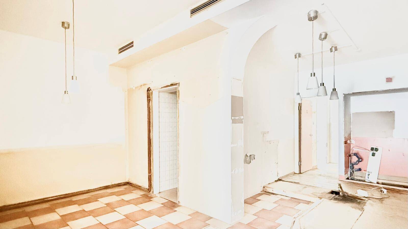 Innenraum in Renovierung mit Fliesenboden, abgehängten Deckenleuchten und sichtbaren Installationsarbeiten.