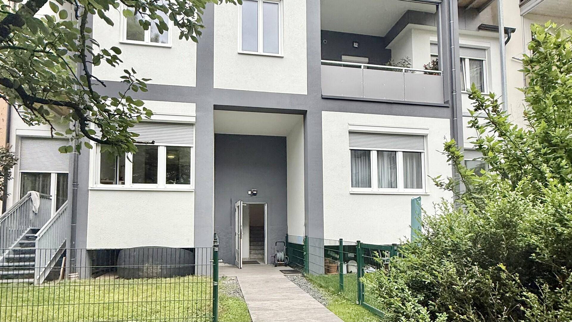 Moderner Eingangsbereich eines Wohnhauses mit Rampe und Zugang zu einem begrünten Gartenbereich.