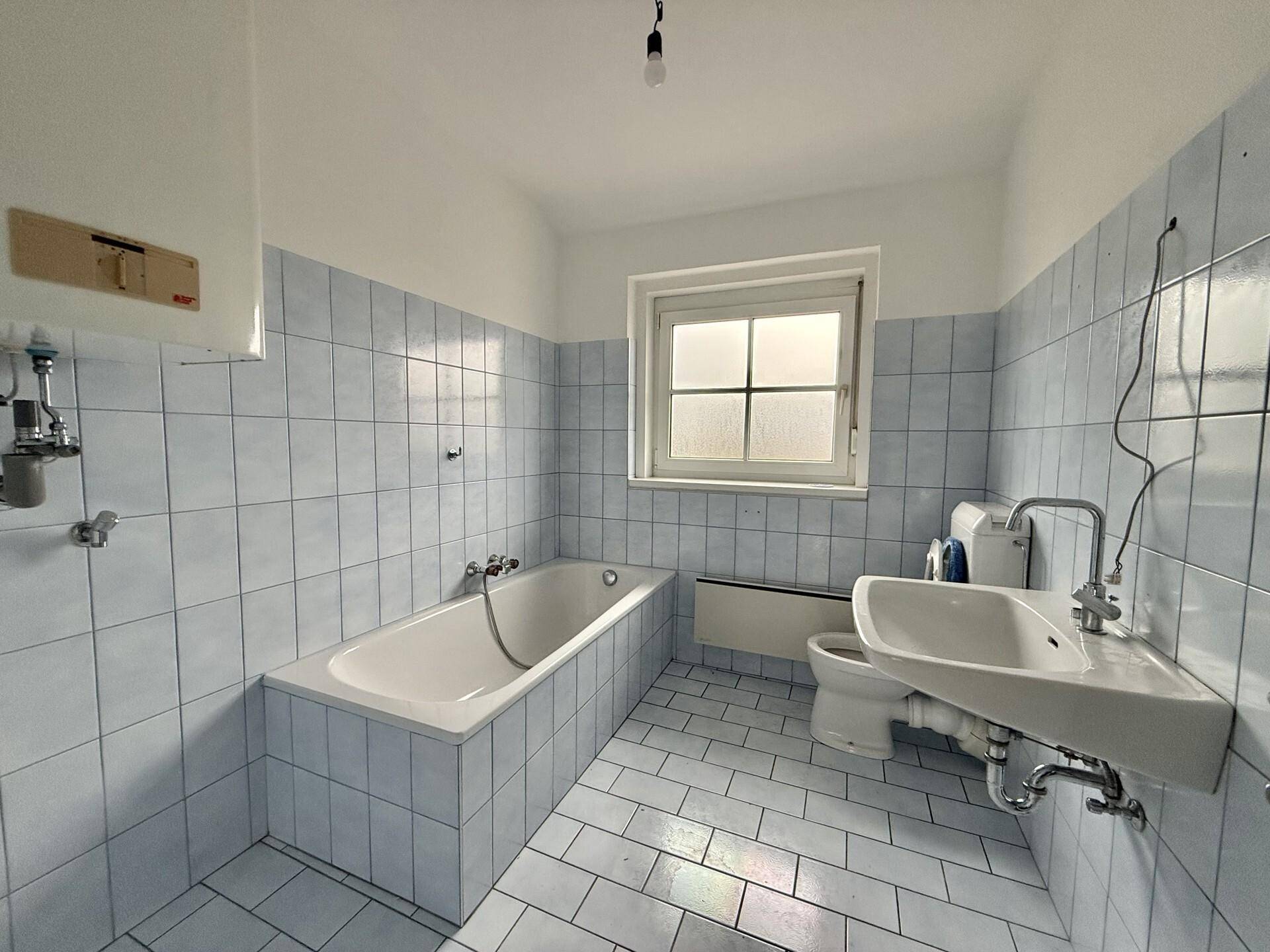 Badezimmer mit hellblauen Fliesen, Badewanne, Waschbecken und Fenster.