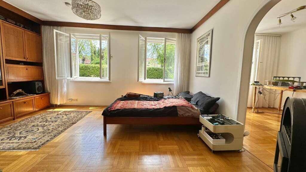 Schlafzimmer mit Holzparkett, Bett und großen Fenstern mit Blick ins Grüne.