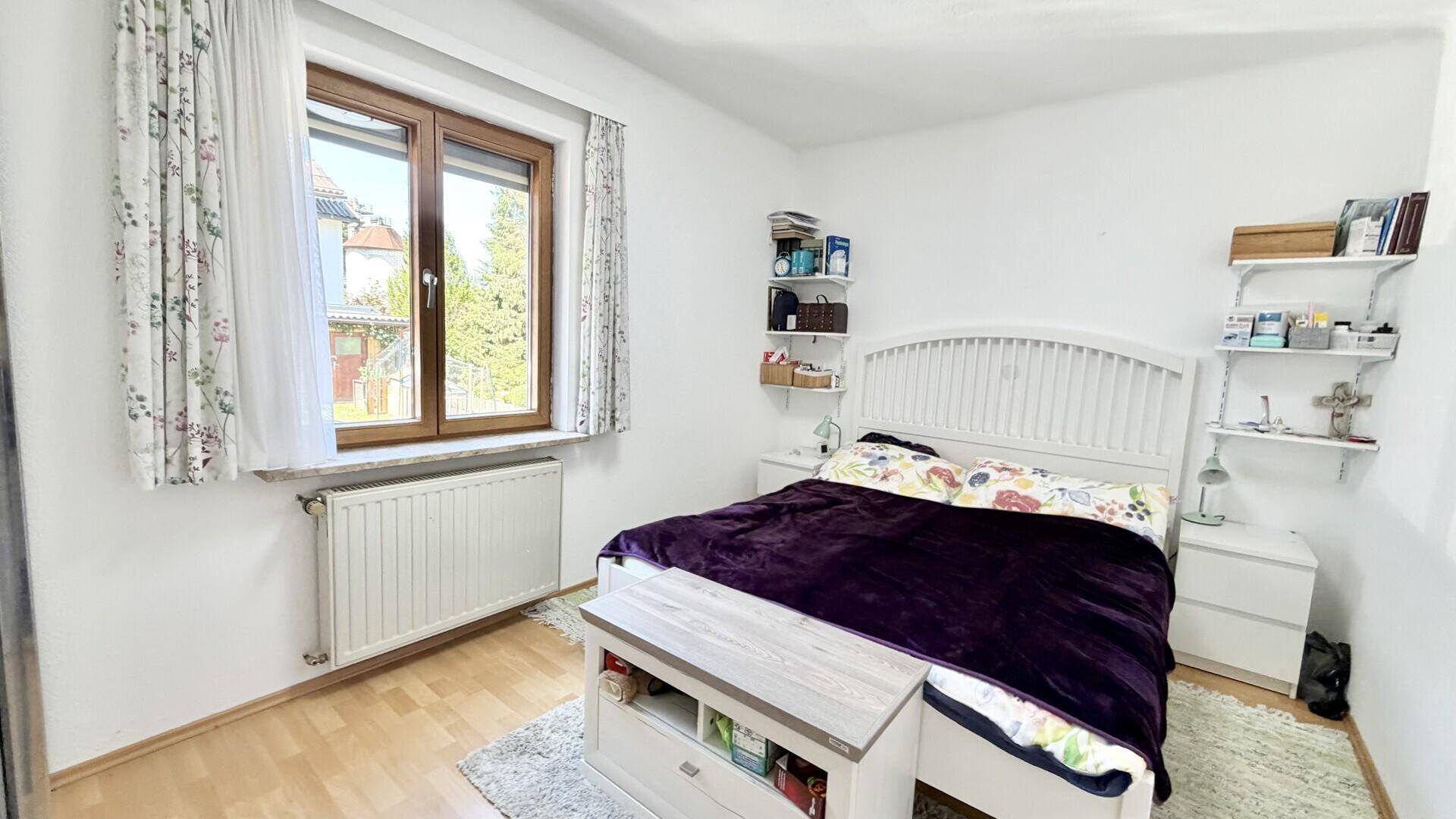 Helles Schlafzimmer mit Doppelbett, Holzboden und Fenster, das viel Tageslicht hereinlässt.