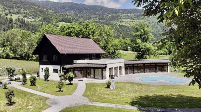 Anwesen mit modernem Anbau, großem Pool und gepflegtem Garten vor einer malerischen Berglandschaft.