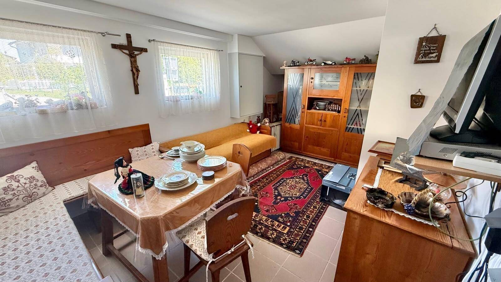 Gemütlicher Essbereich mit traditionellen Holzmöbeln, Teppich und Fenstern mit viel Tageslicht.