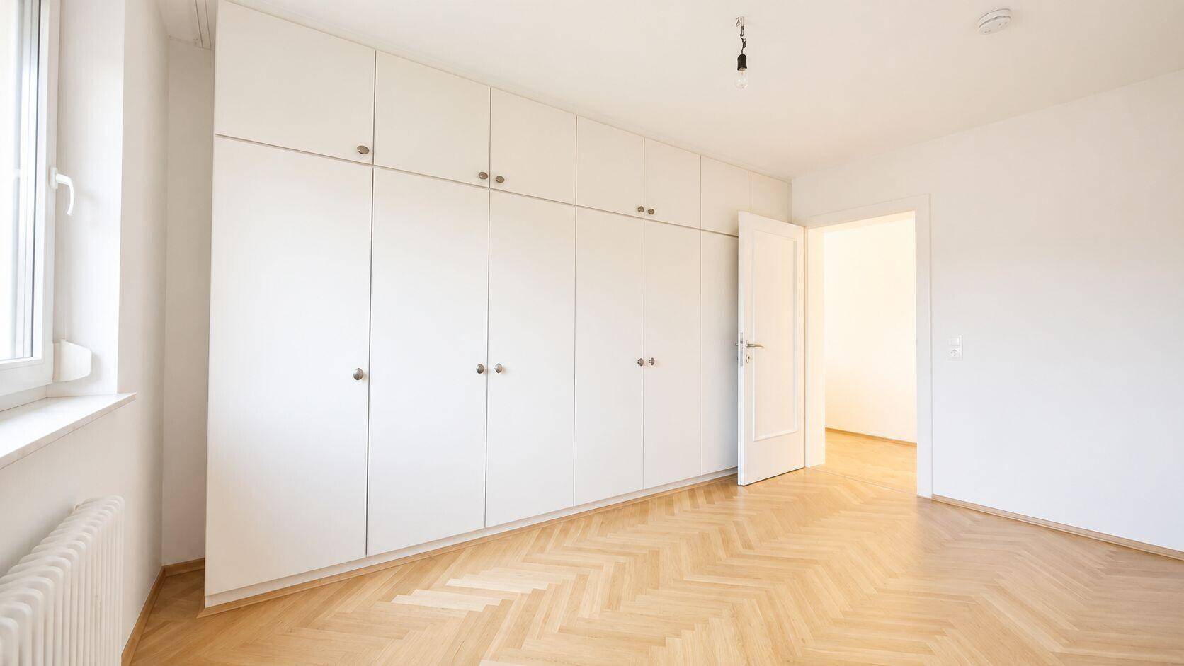 Schlafzimmer mit Einbauschränken und hellem Fischgrät-Parkettboden.