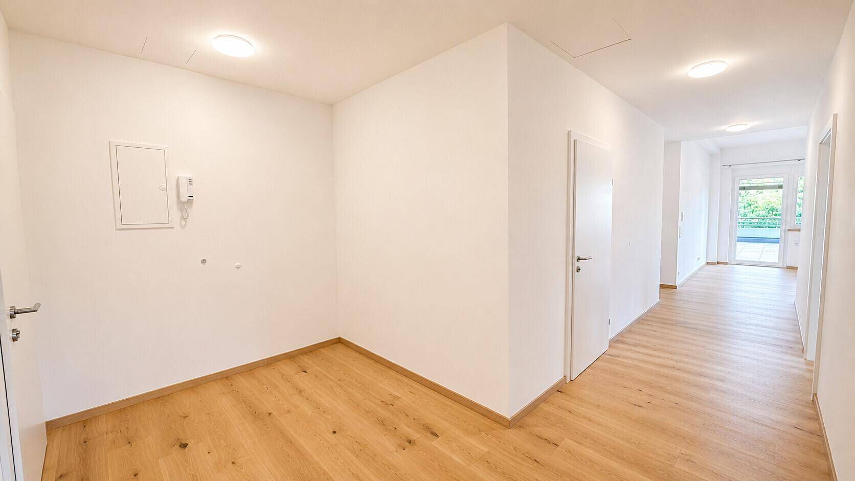 Heller Flur mit Holzboden und weißen Wänden, der zu verschiedenen Räumen der Wohnung führt.