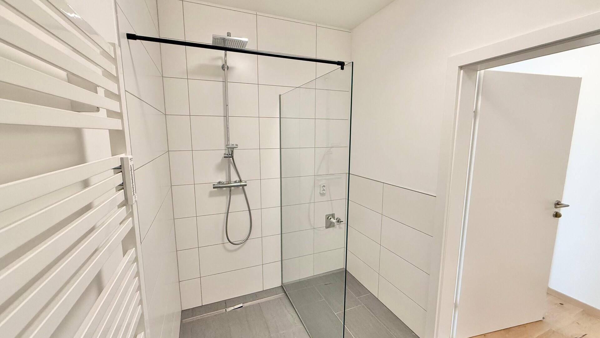 Elegante begehbare Dusche mit Regenduschkopf in einem modernen Badezimmer mit Fliesenboden.