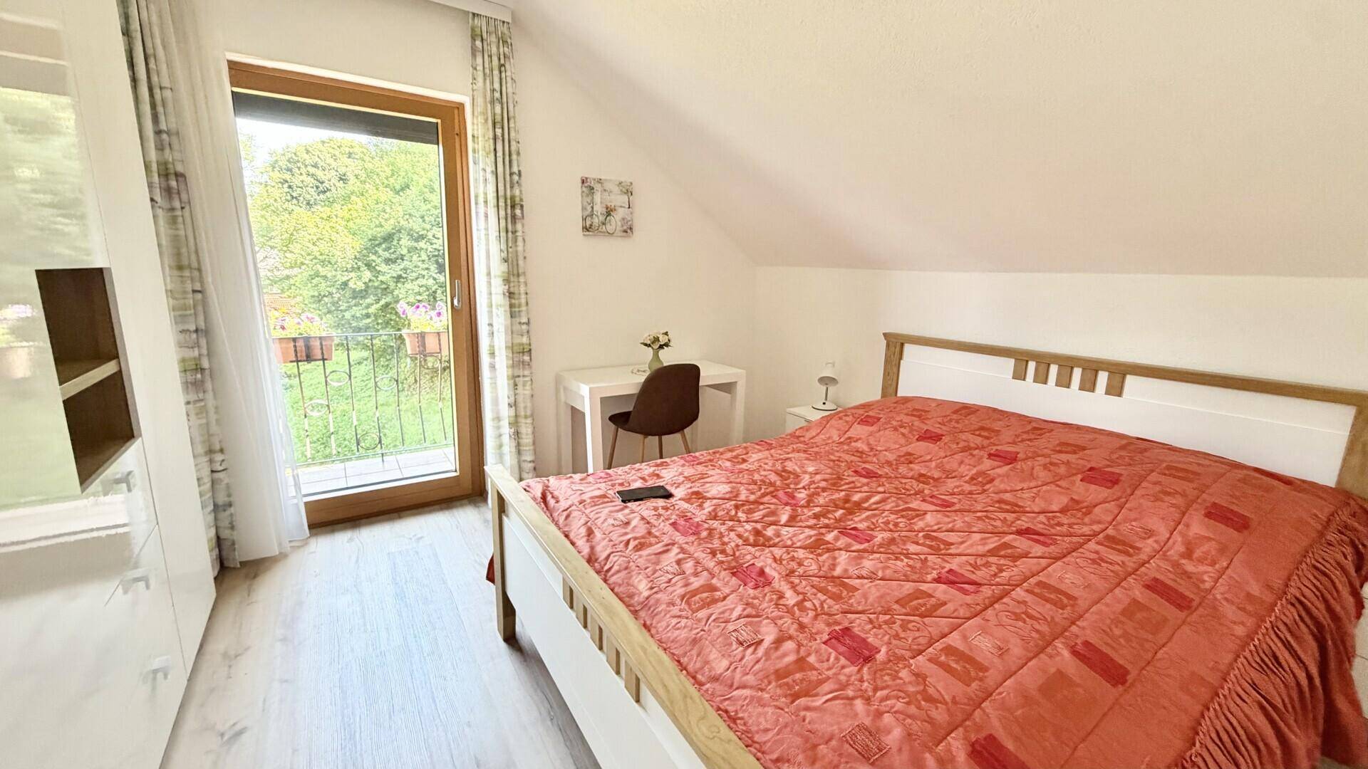 Helles Schlafzimmer im Dachgeschoss mit Doppelbett, Schreibtisch und Zugang zum Balkon.