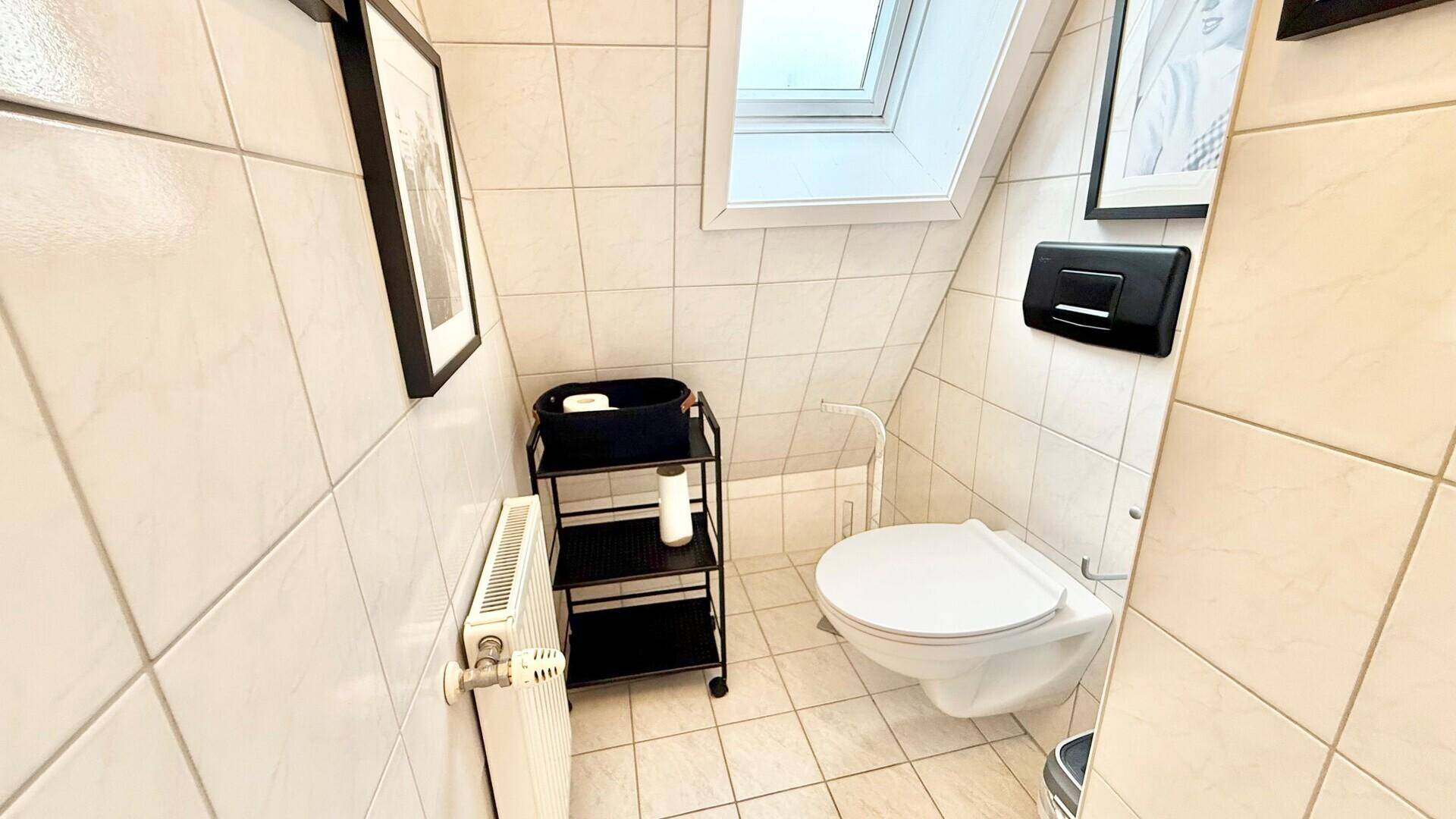 Kleines WC mit Dachfenster, weißen Fliesen und Wand-WC.