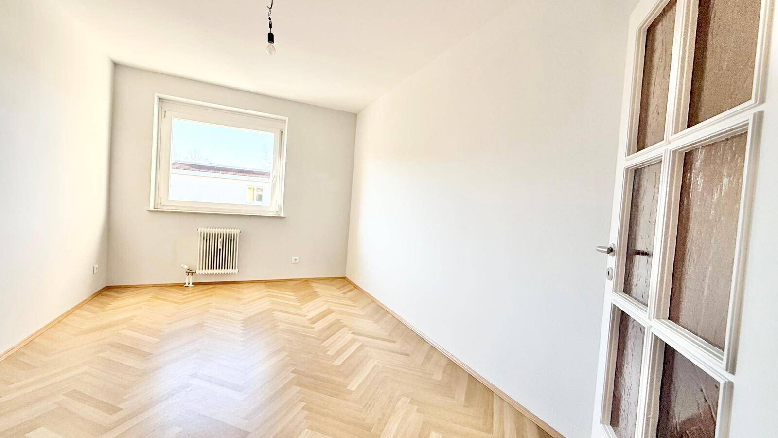 Helles Zimmer mit Fischgrät-Parkett und einer Tür mit Glaseinsätzen.