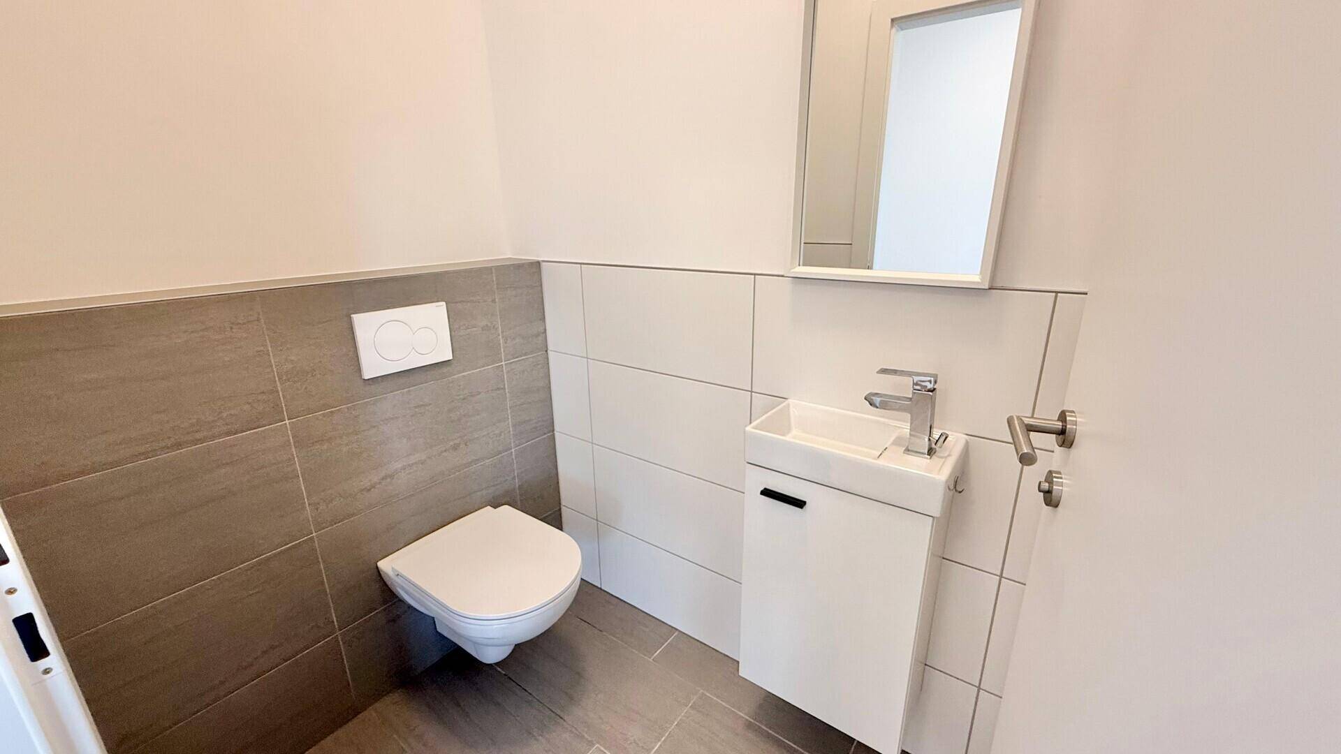 Modernes Gäste-WC mit wandhängender Toilette und kleinem Waschbecken, in neutralen Farben gefliest.