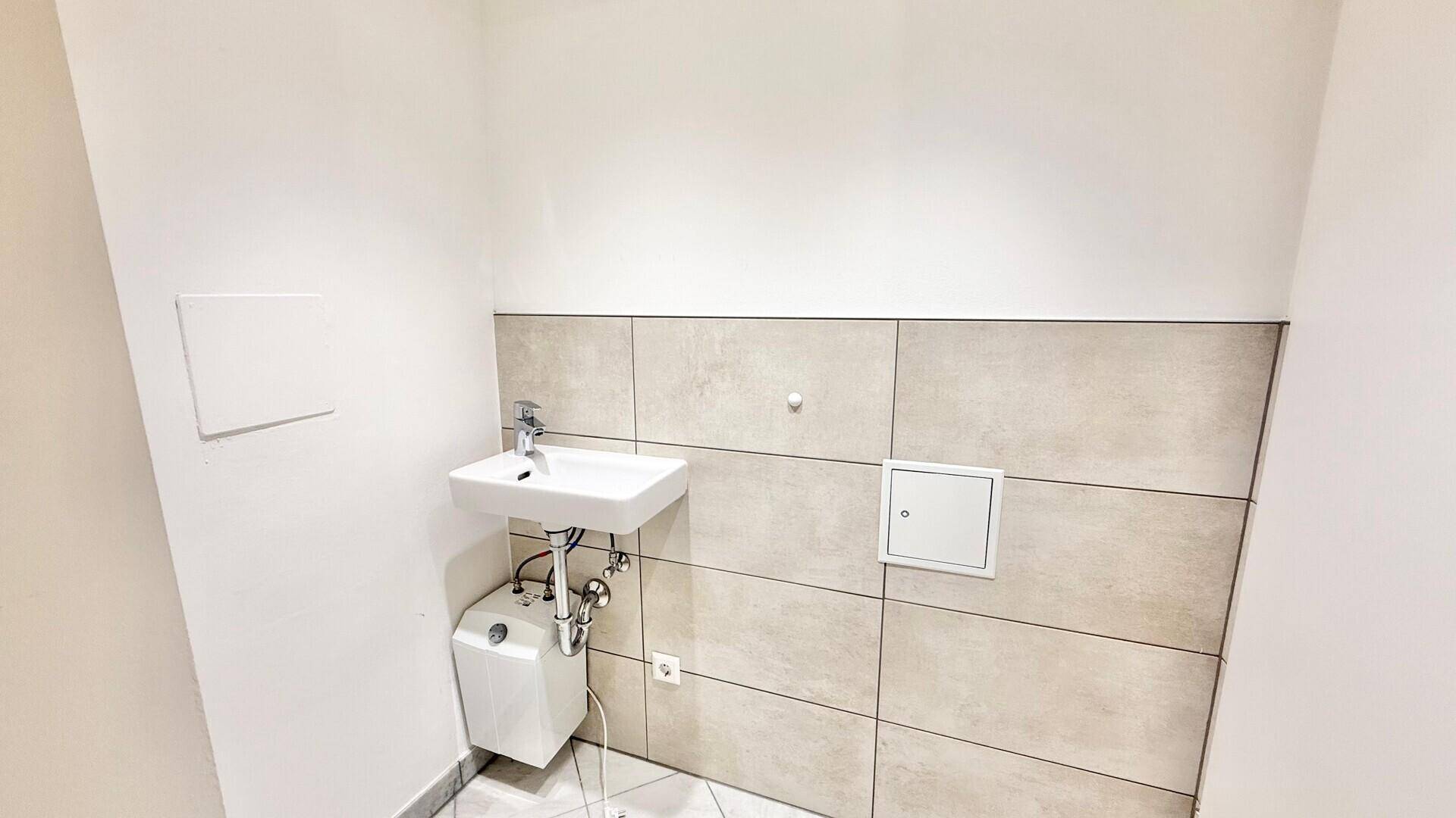 Kleines Badezimmer mit Waschbecken, beigefarbenen Wandfliesen und einem Untertischgerät.