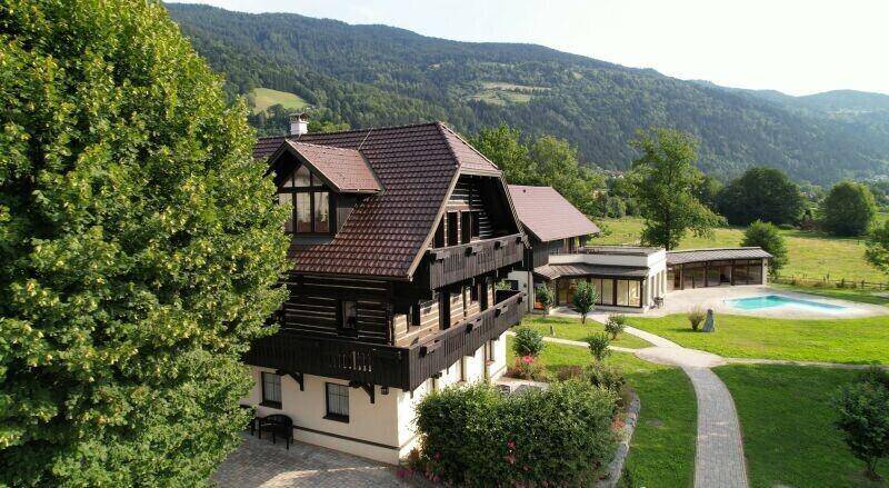 Großzügige Außenanlage mit traditionellem Gebäude, Pool und weitläufigen Grünflächen vor einer Bergkulisse.