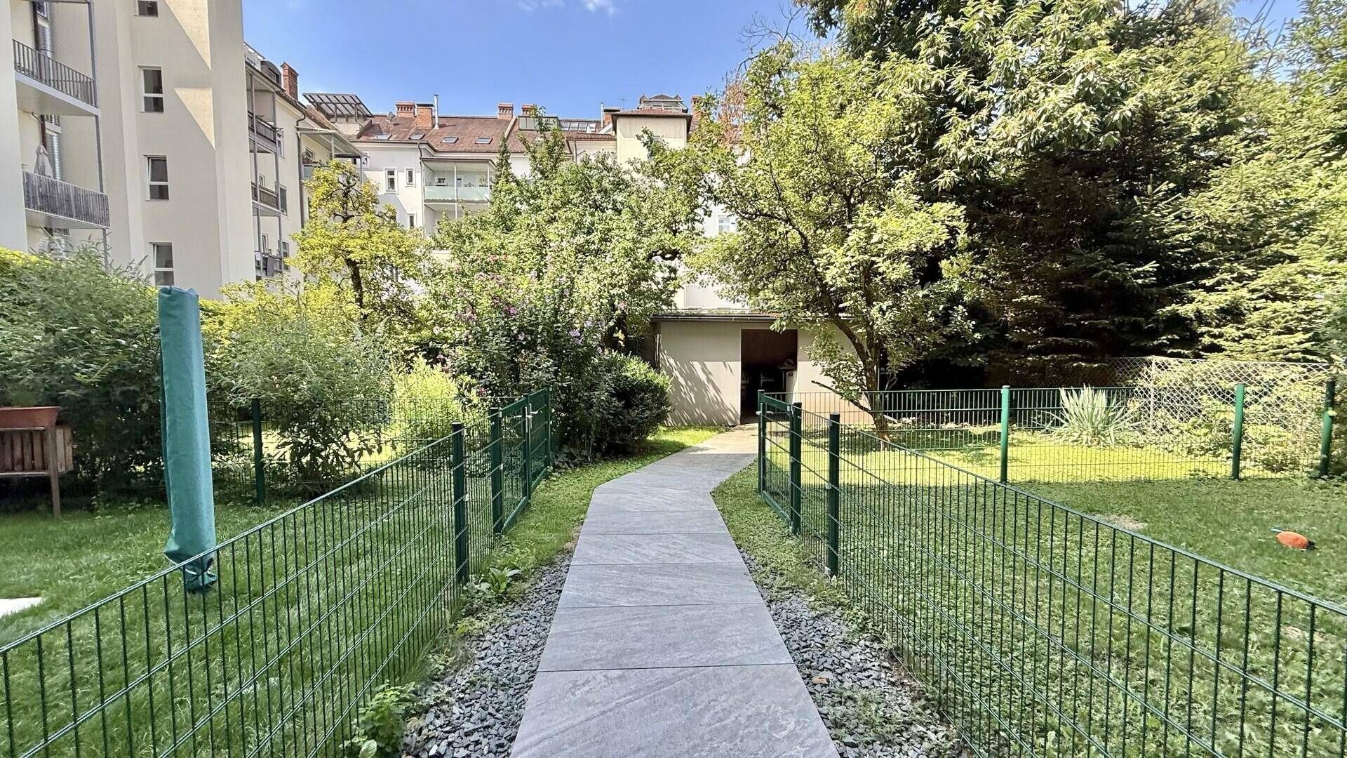 Langer Gartenweg durch eine grüne Anlage, der zu einem kleinen Schuppen führt.