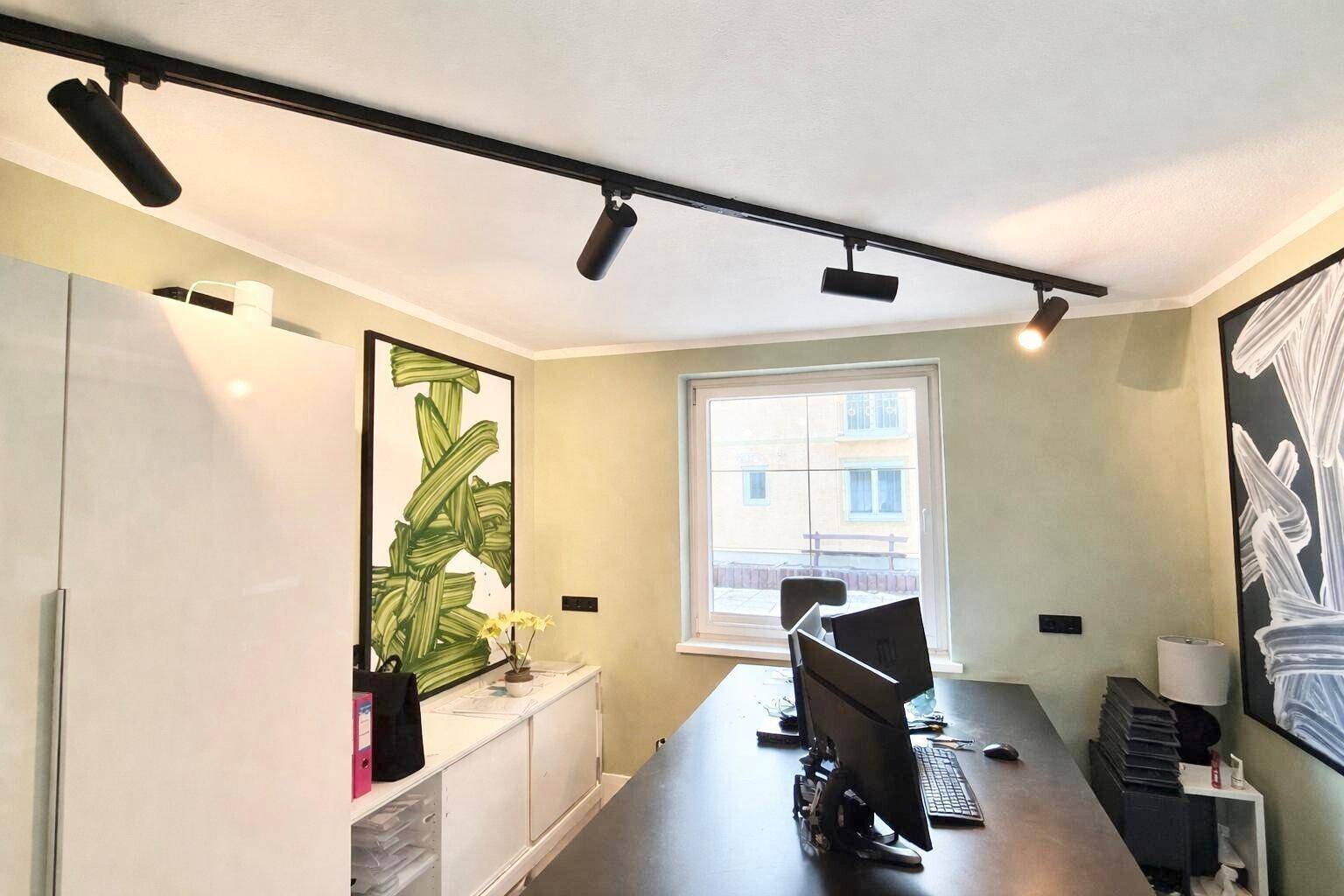 Modern eingerichtetes Büro mit Schreibtisch, Stauraum und Deckenstrahlern für gute Beleuchtung.