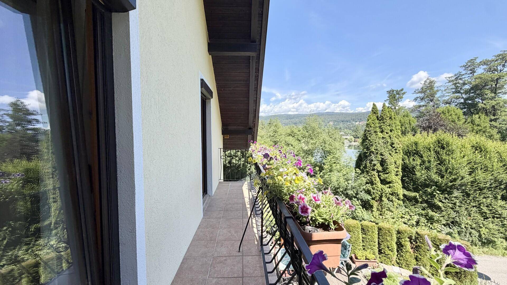 Langer Balkon mit Blumenkästen und weitem Blick auf den See und die umliegende Landschaft.