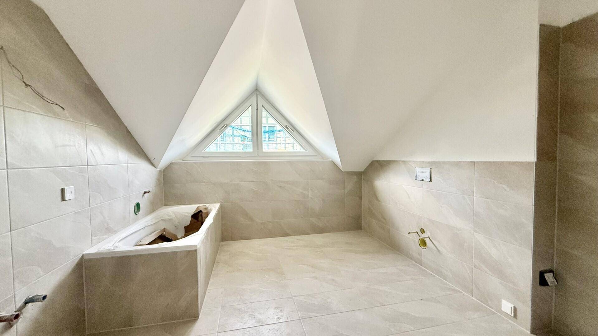 Badezimmer im Bau mit Fliesenboden, eingebauter Badewanne und Dachfenster.