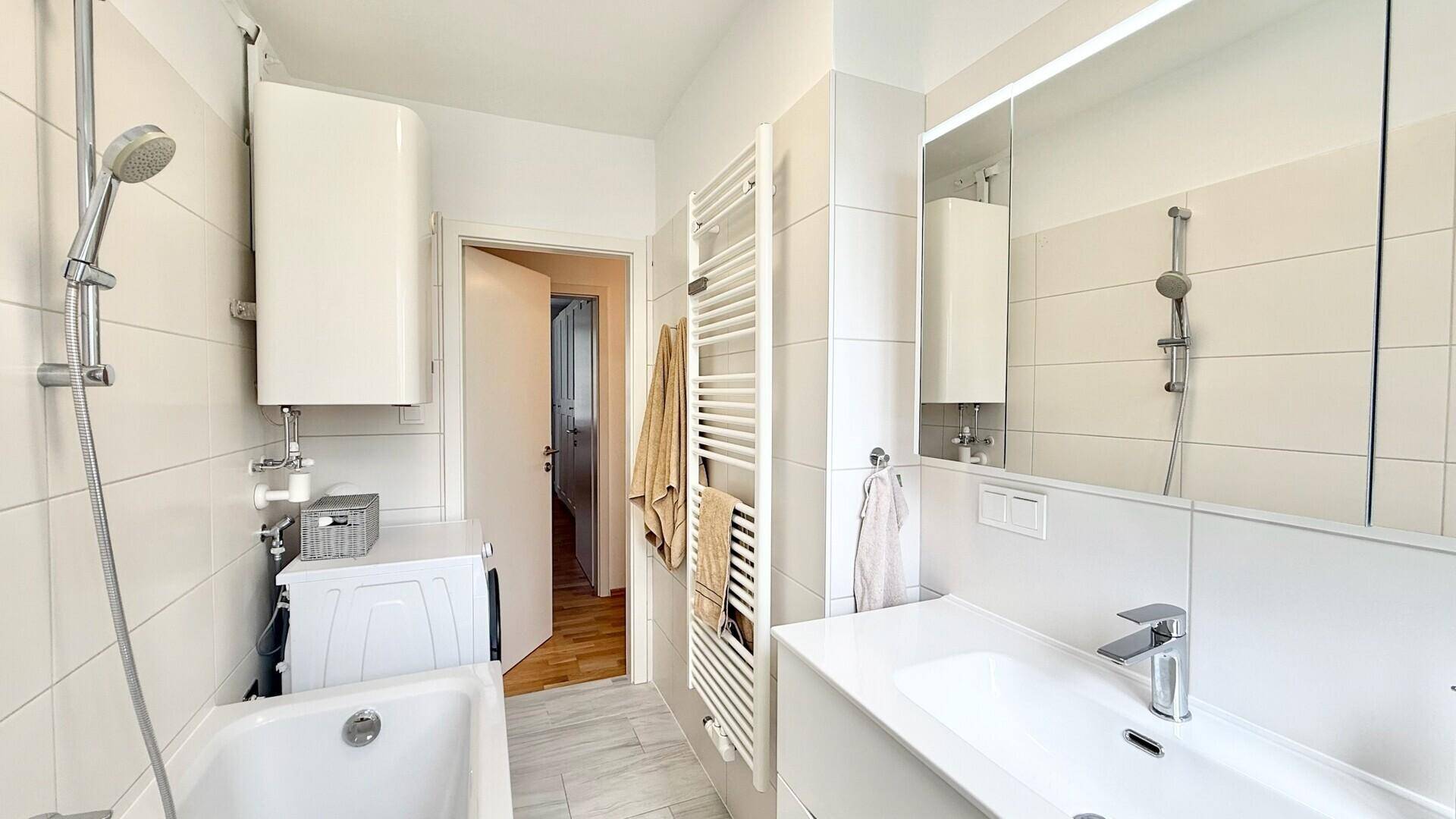 Helles Badezimmer mit Badewanne, Waschmaschine und Handtuchheizkörper.