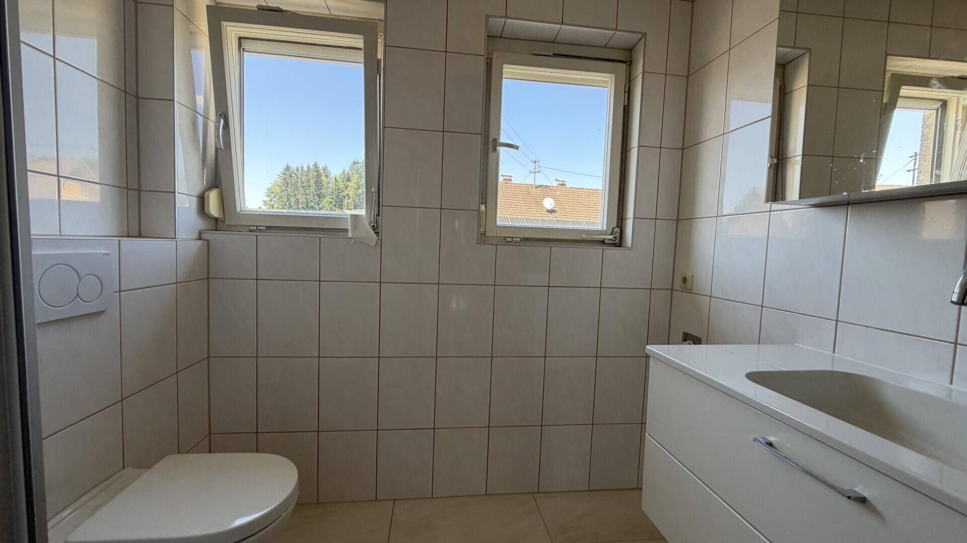 Helles Badezimmer mit weißen Fliesen, WC und modernem Waschtisch.