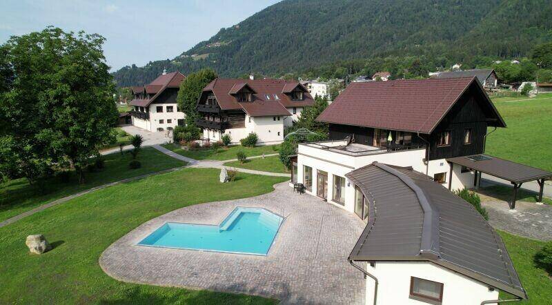 Weitläufiges Anwesen mit mehreren Gebäuden, einem großen Pool und gepflegten Grünflächen vor einer Bergkulisse.