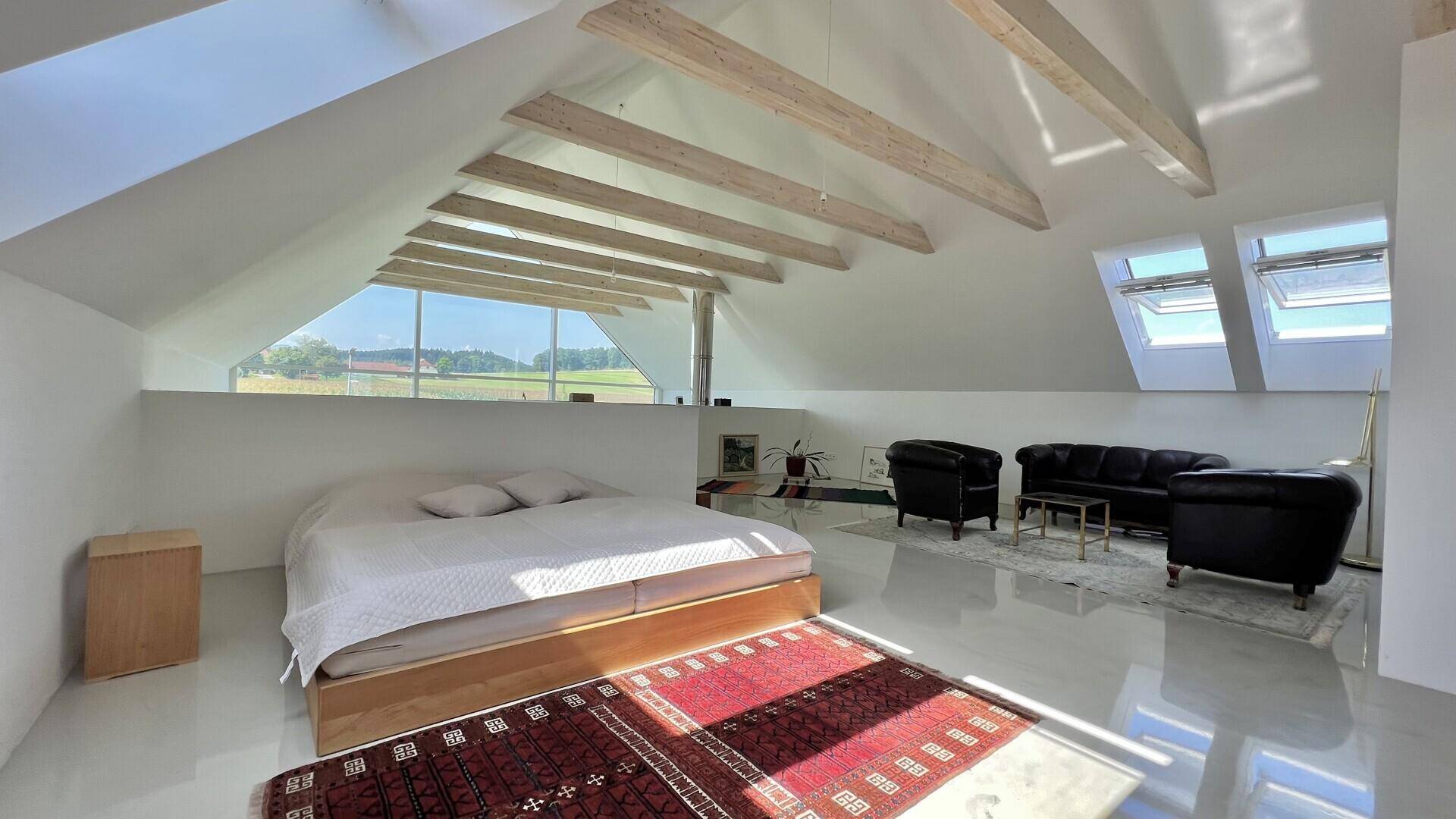 Helles Schlafzimmer im Dachgeschoss mit freiliegenden Holzbalken und Dachfenstern.