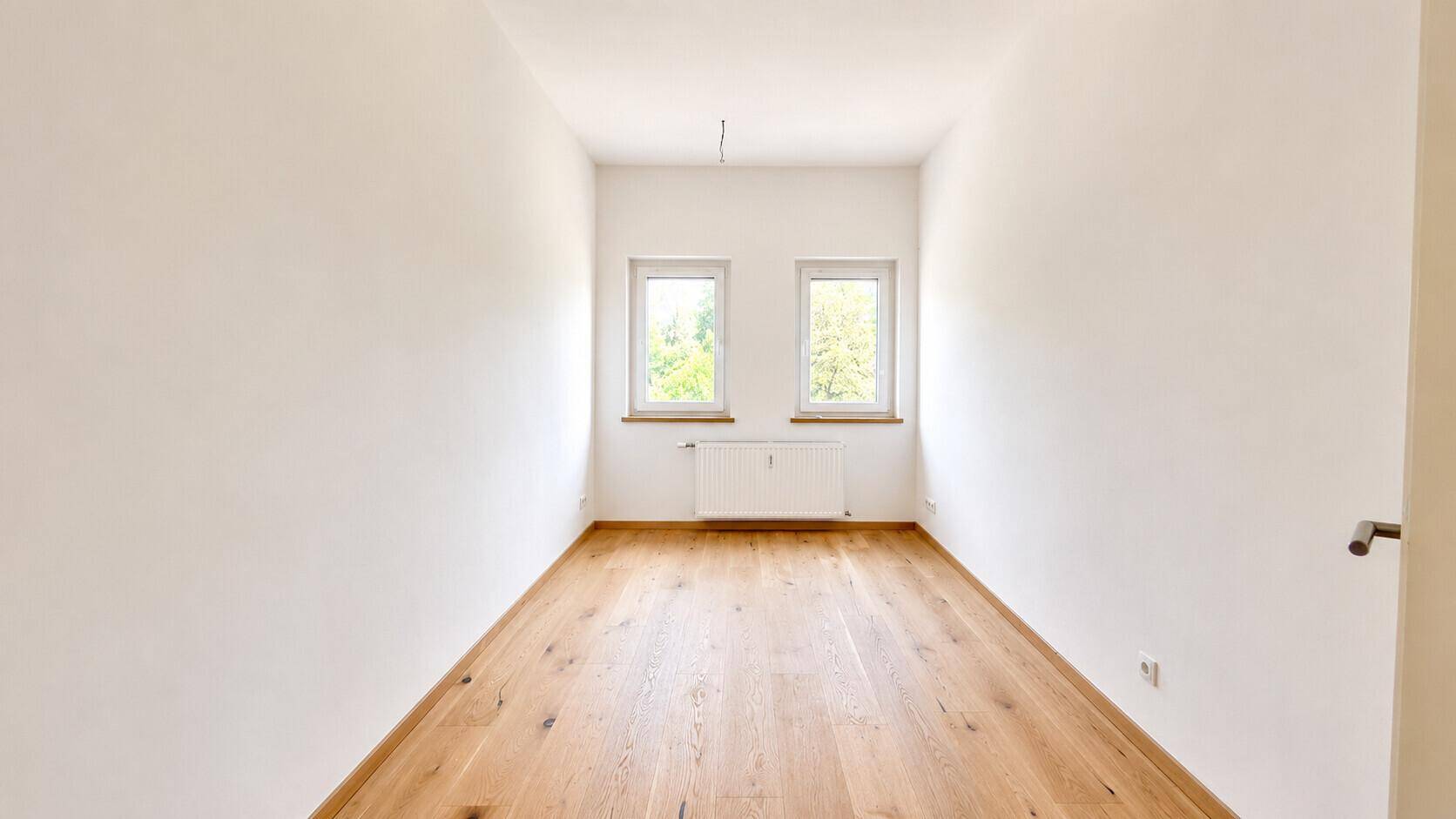 Geräumiges Zimmer mit viel Tageslicht, hellem Holzboden und Blick auf die umliegende Natur.