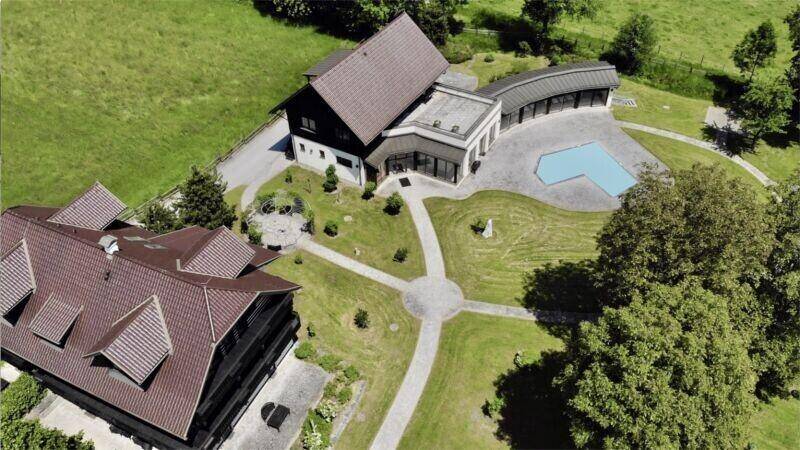 Luftaufnahme eines weitläufigen Anwesens mit mehreren Gebäuden, Pool und gepflegten Grünflächen in den Bergen.