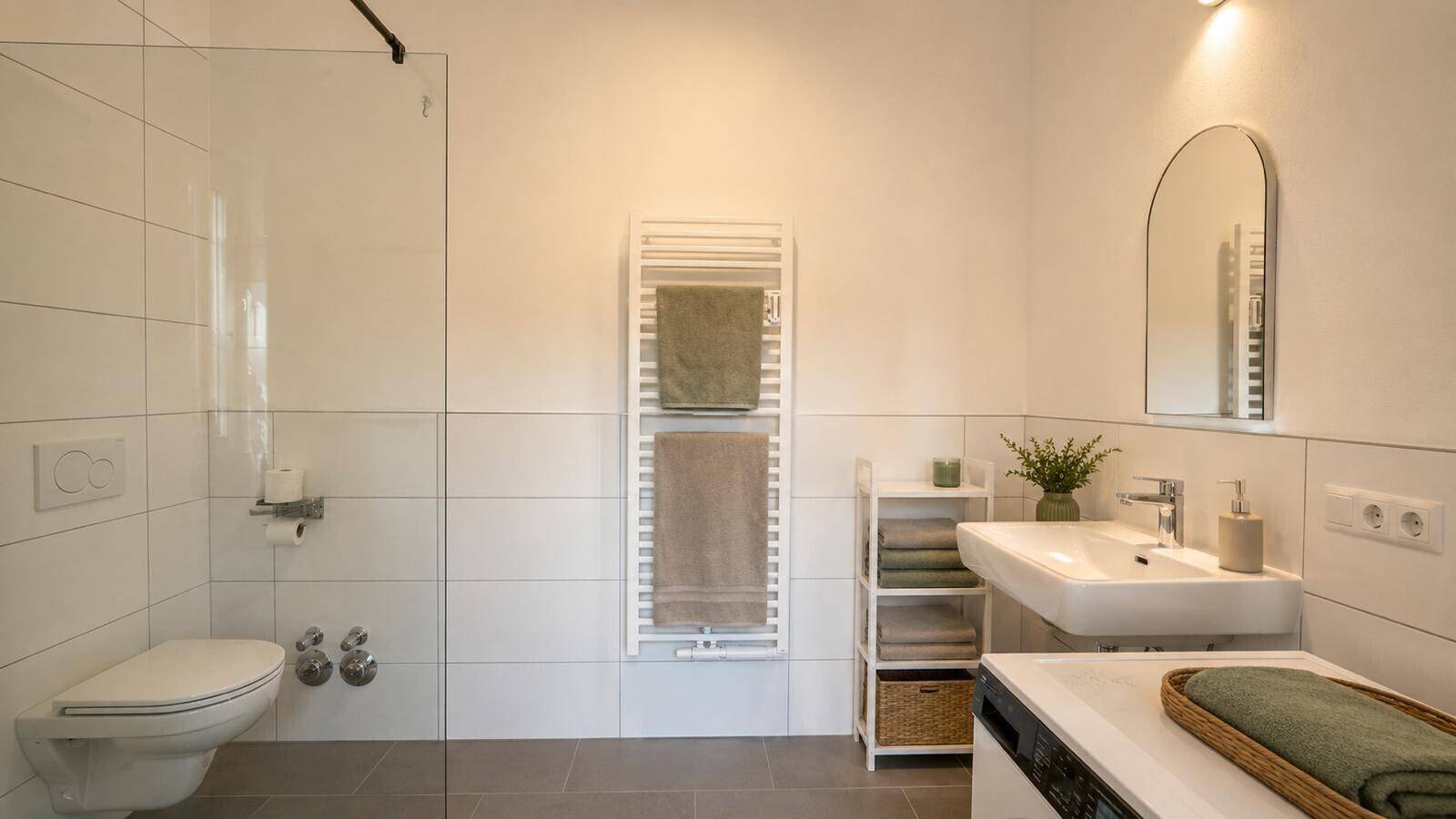 Modernes Badezimmer mit ebenerdiger Dusche, wandhängendem WC und beheiztem Handtuchhalter.
