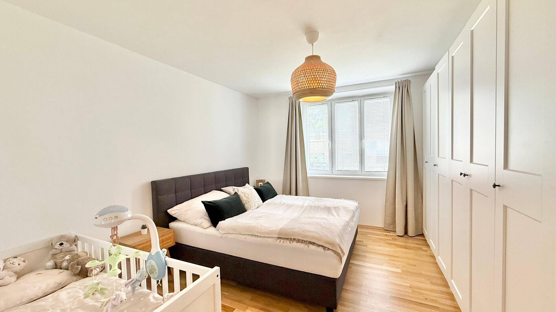 Helles Schlafzimmer mit Doppelbett, Babybett und großem Kleiderschrank.