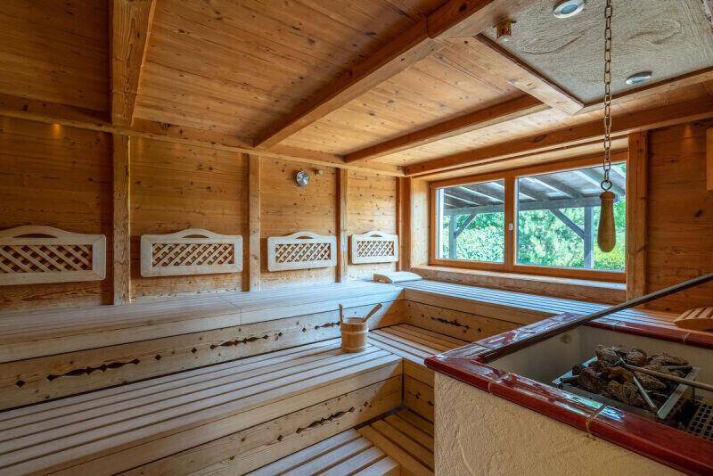 Geräumige Holzsauna mit breiten Bänken, großem Fenster und traditionellem Saunaofen, bietet viel Platz zum Entspannen.
