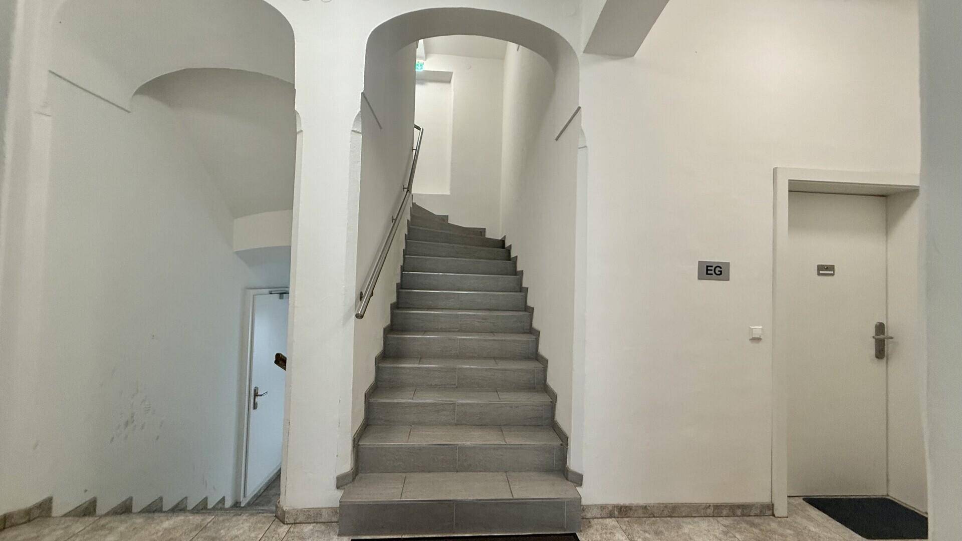Helles Treppenhaus mit Fliesenboden und Zugang zu den Wohnungen im Erdgeschoss.