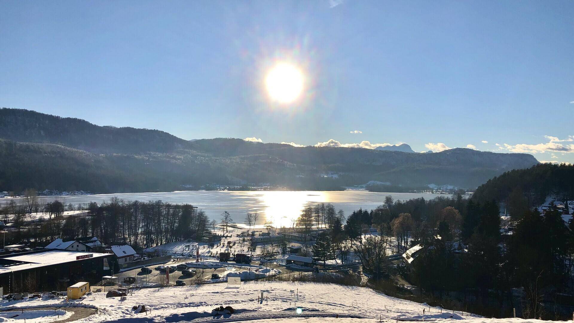 Winterlandschaft mit zugefrorenem See, schneebedeckten Bergen und strahlendem Sonnenschein.