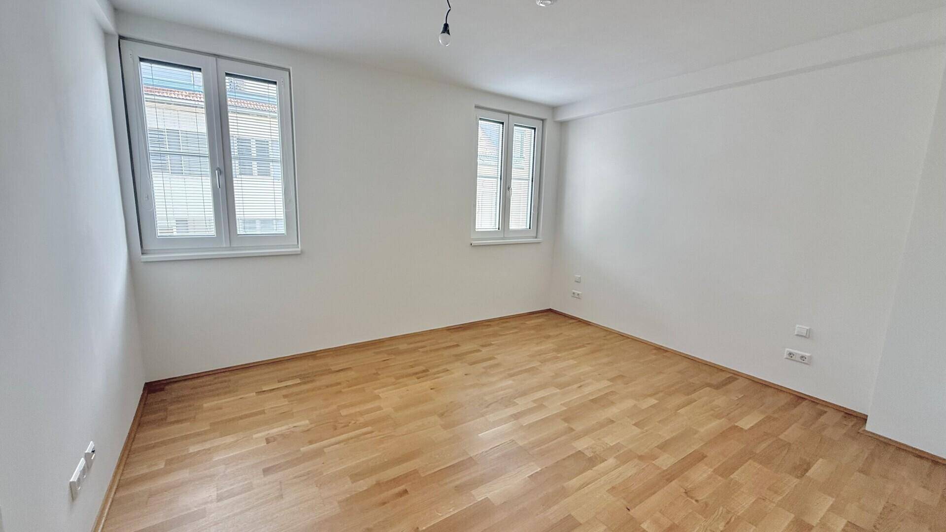 Helles Zimmer mit Parkettboden und zwei Fenstern, ideal als Schlaf- oder Arbeitszimmer.