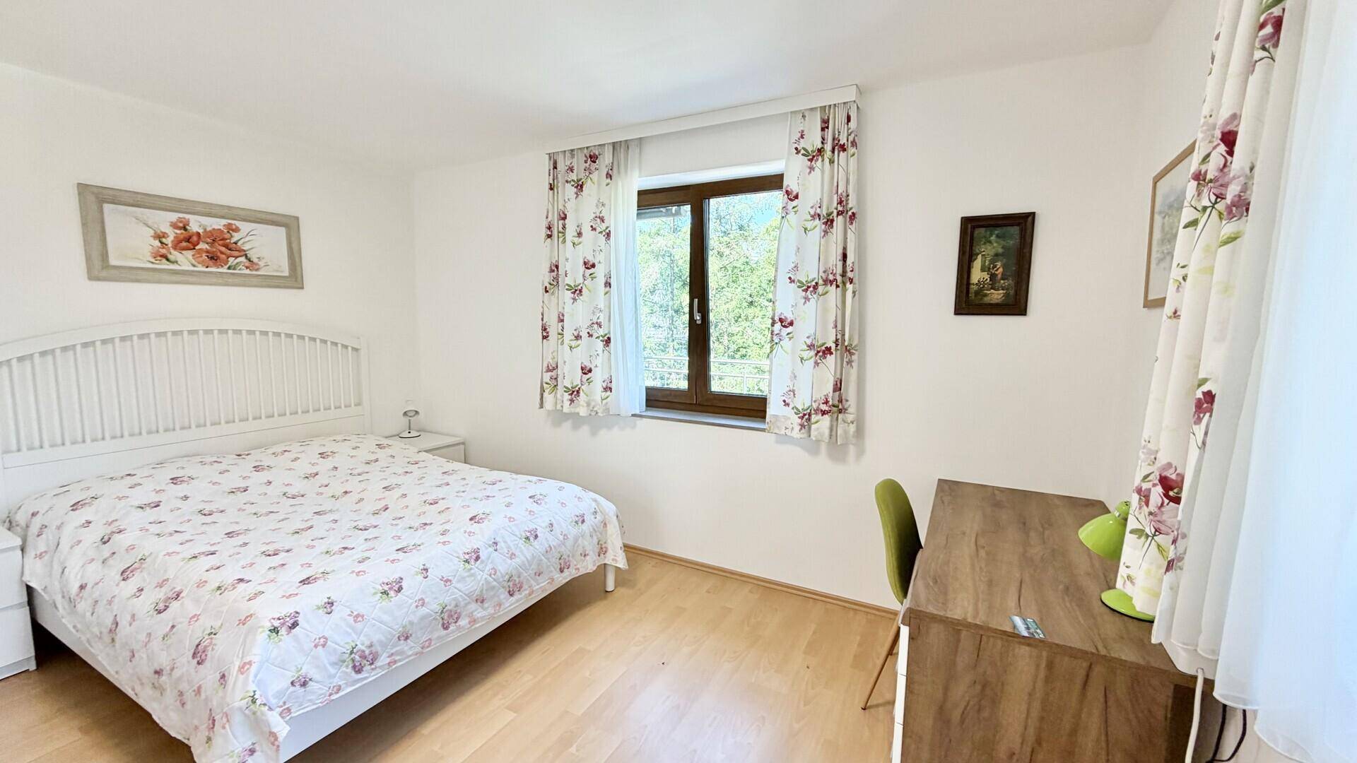 Helles Schlafzimmer mit Doppelbett, Holzboden und Fenster mit Blick ins Grüne.