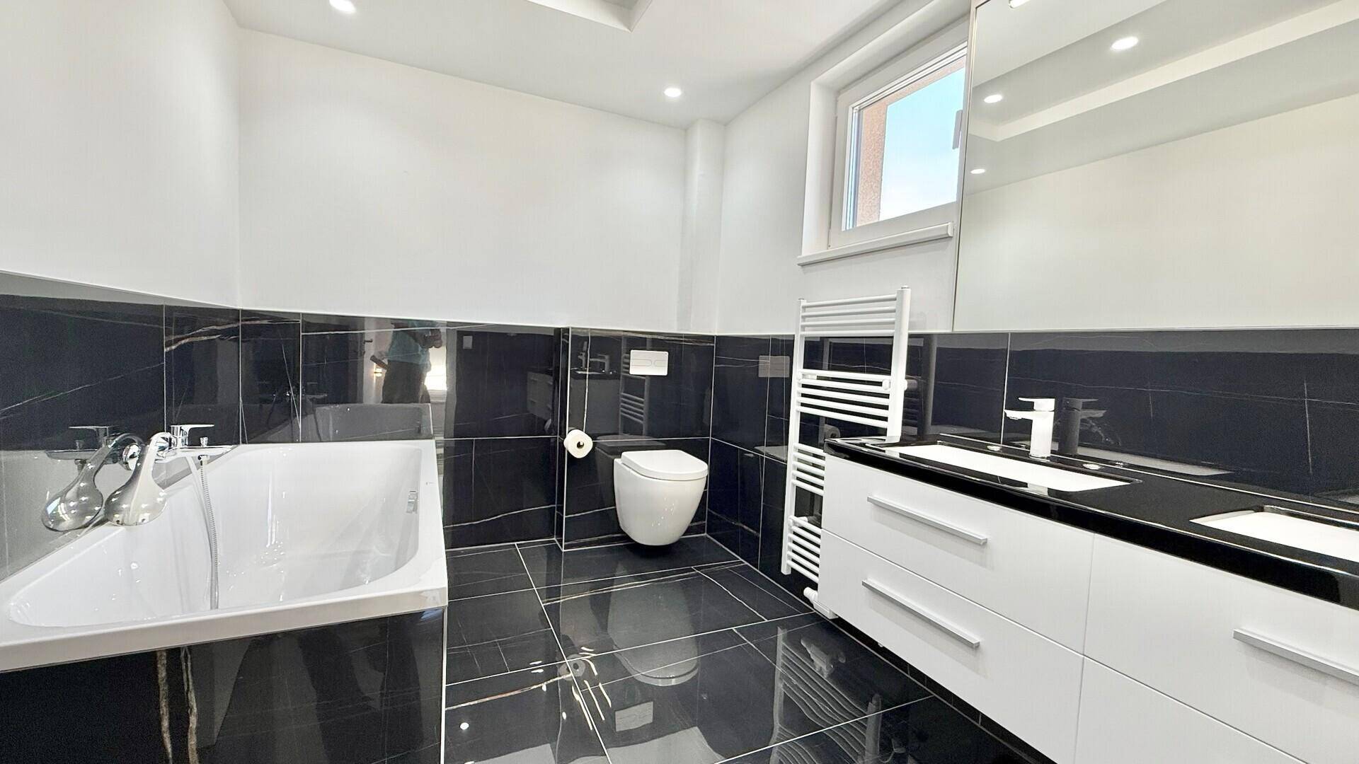 Elegantes Badezimmer mit schwarzen Fliesen, Badewanne, Doppelwaschbecken und großem Spiegelschrank.