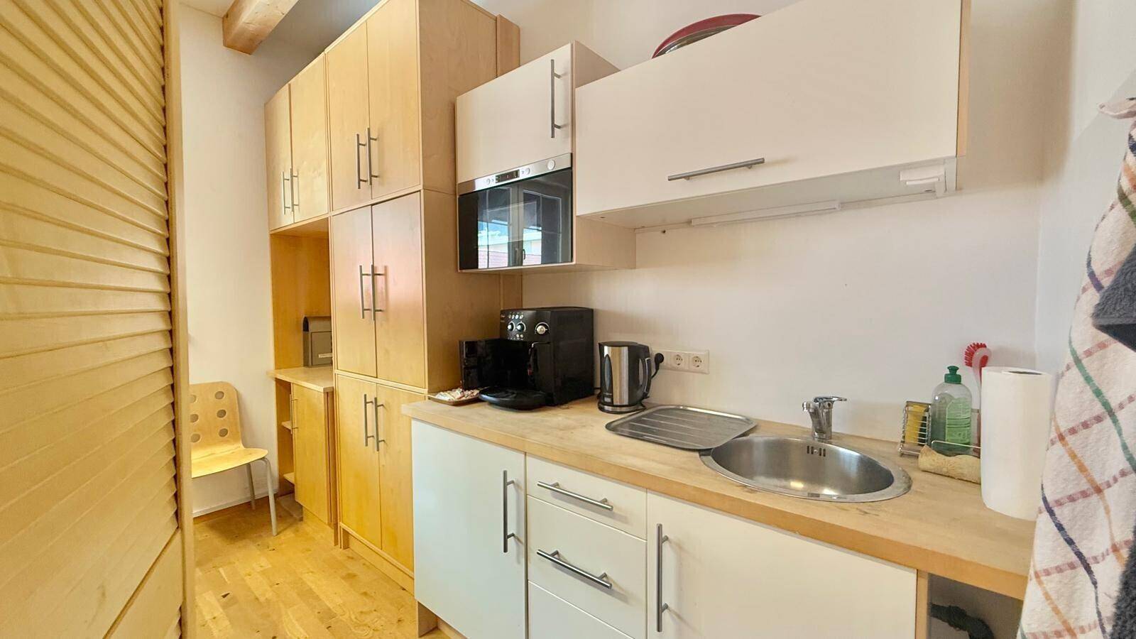 Kleine, funktionale Küchenzeile mit Spüle, Mikrowelle und Kaffeemaschine in hellem Holzdesign, praktisch und kompakt.