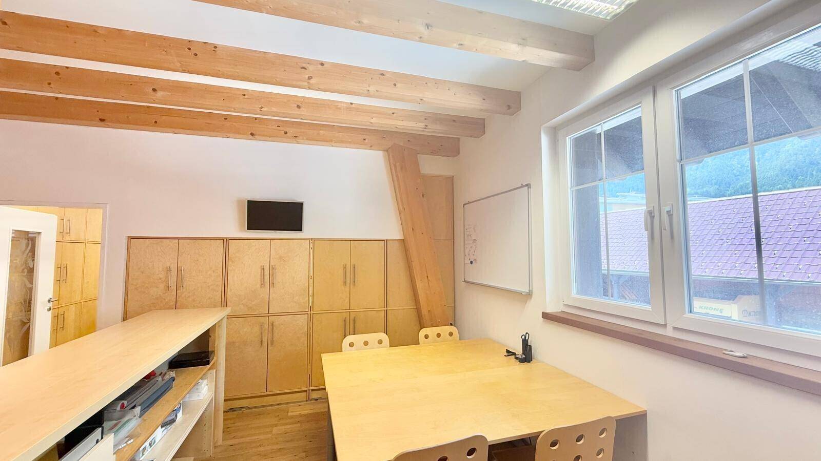 Geräumiges Büro mit Holzbalkendecke, großen Fenstern und mehreren Arbeitsplätzen, bietet eine helle Arbeitsumgebung.