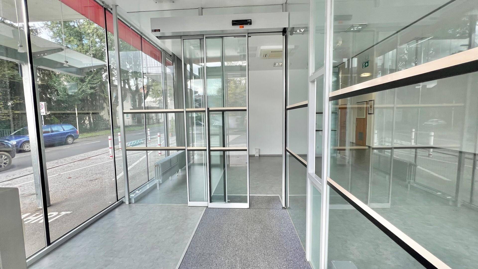Heller Eingangsbereich eines Geschäfts mit großen Glasfronten und automatischen Schiebetüren zur Straße hin.