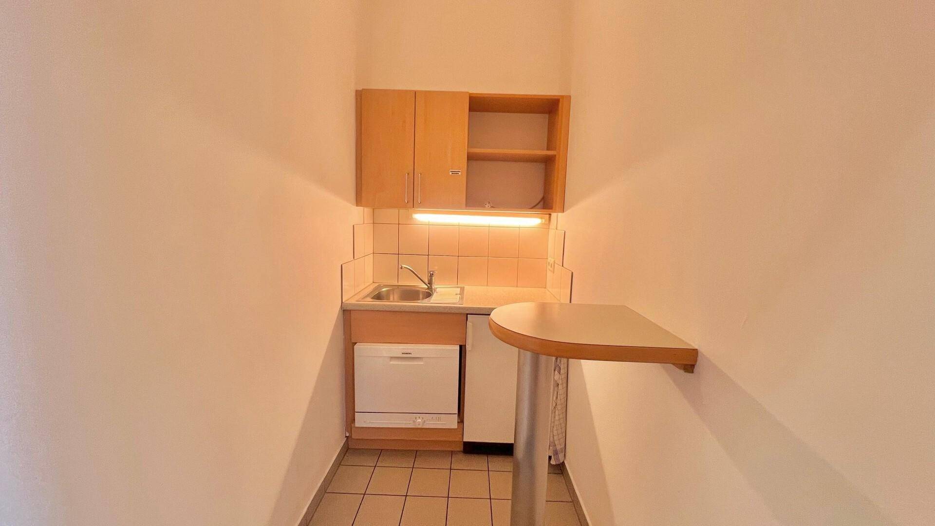 Kleine Küchenzeile mit Spüle, Unterschränken, Geschirrspüler und einem Bartresen in hellem Design.