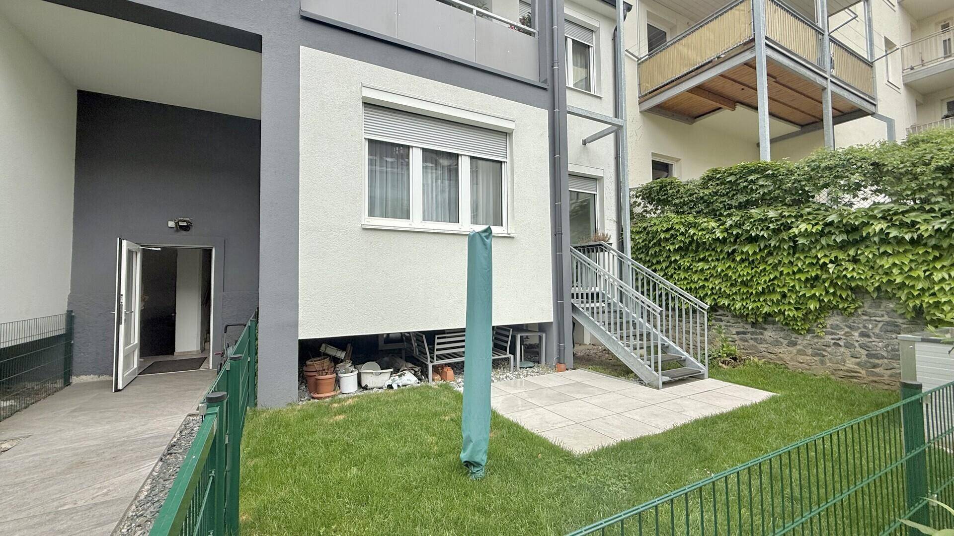 Gepflegter Gartenbereich mit Rasenfläche, kleiner Terrasse und Zugang zum Gebäude.