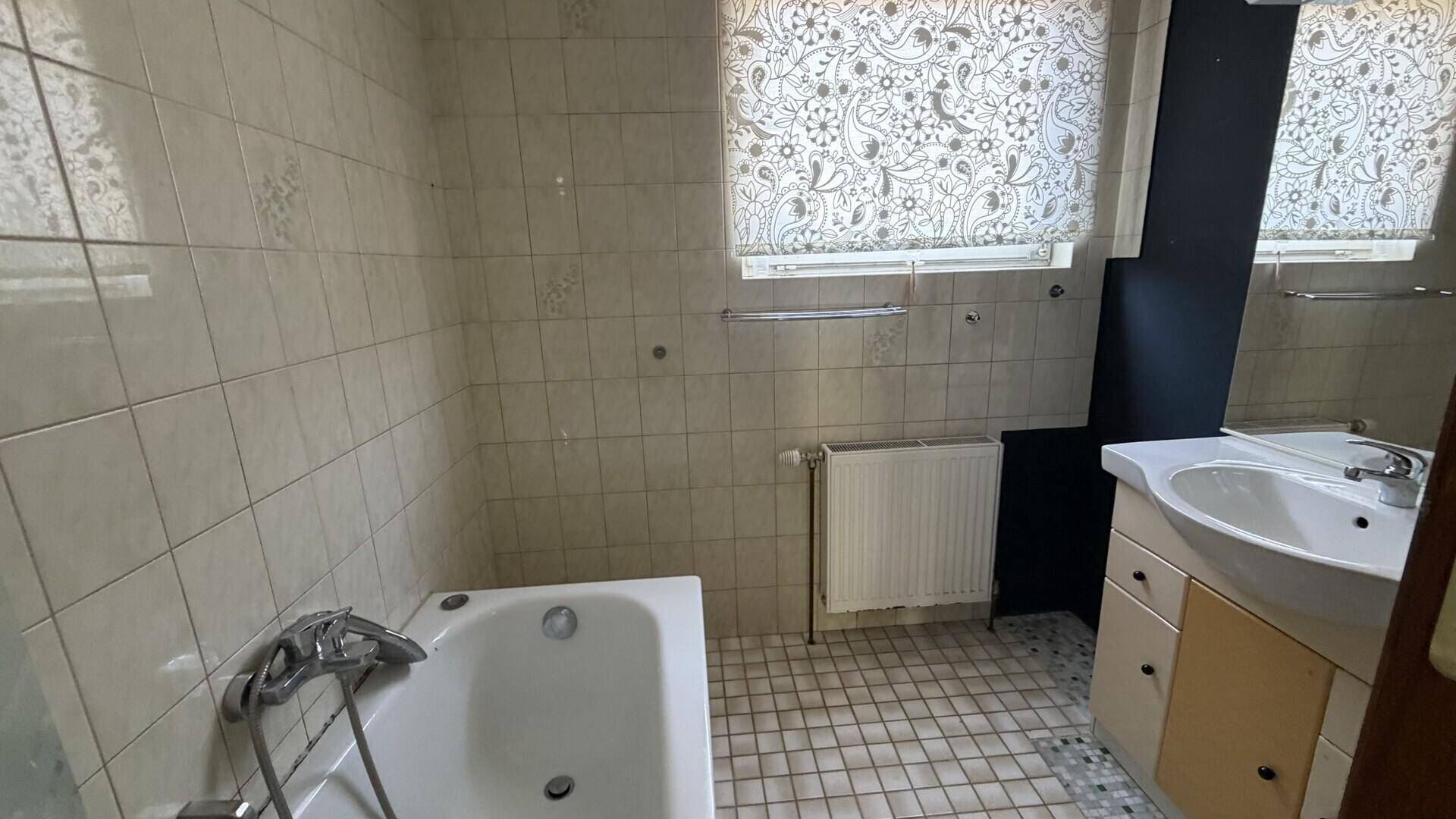 Gefliestes Badezimmer mit Badewanne, Waschbecken und Fenster.