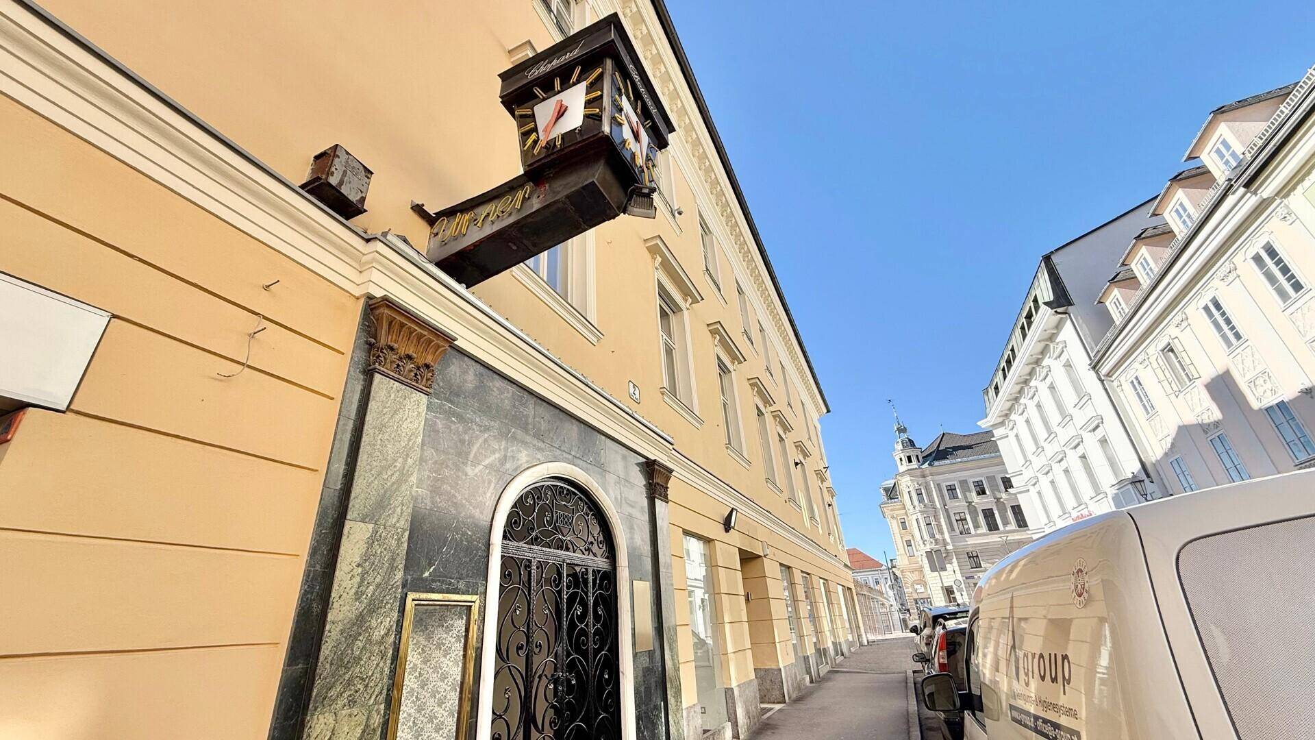Historisches Gebäude mit gelber Fassade und schmiedeeisernem Eingangstor an einer belebten Straße.