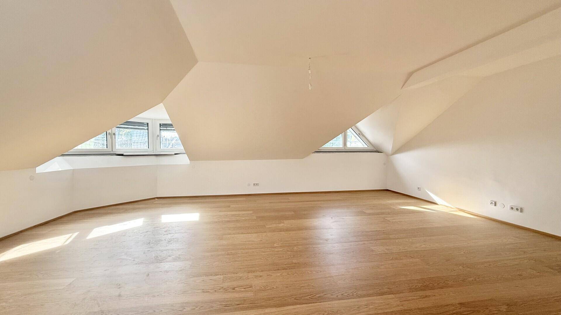 Leerer Raum im Dachgeschoss mit Holzboden und schrägen Wänden, bereit zur individuellen Gestaltung.