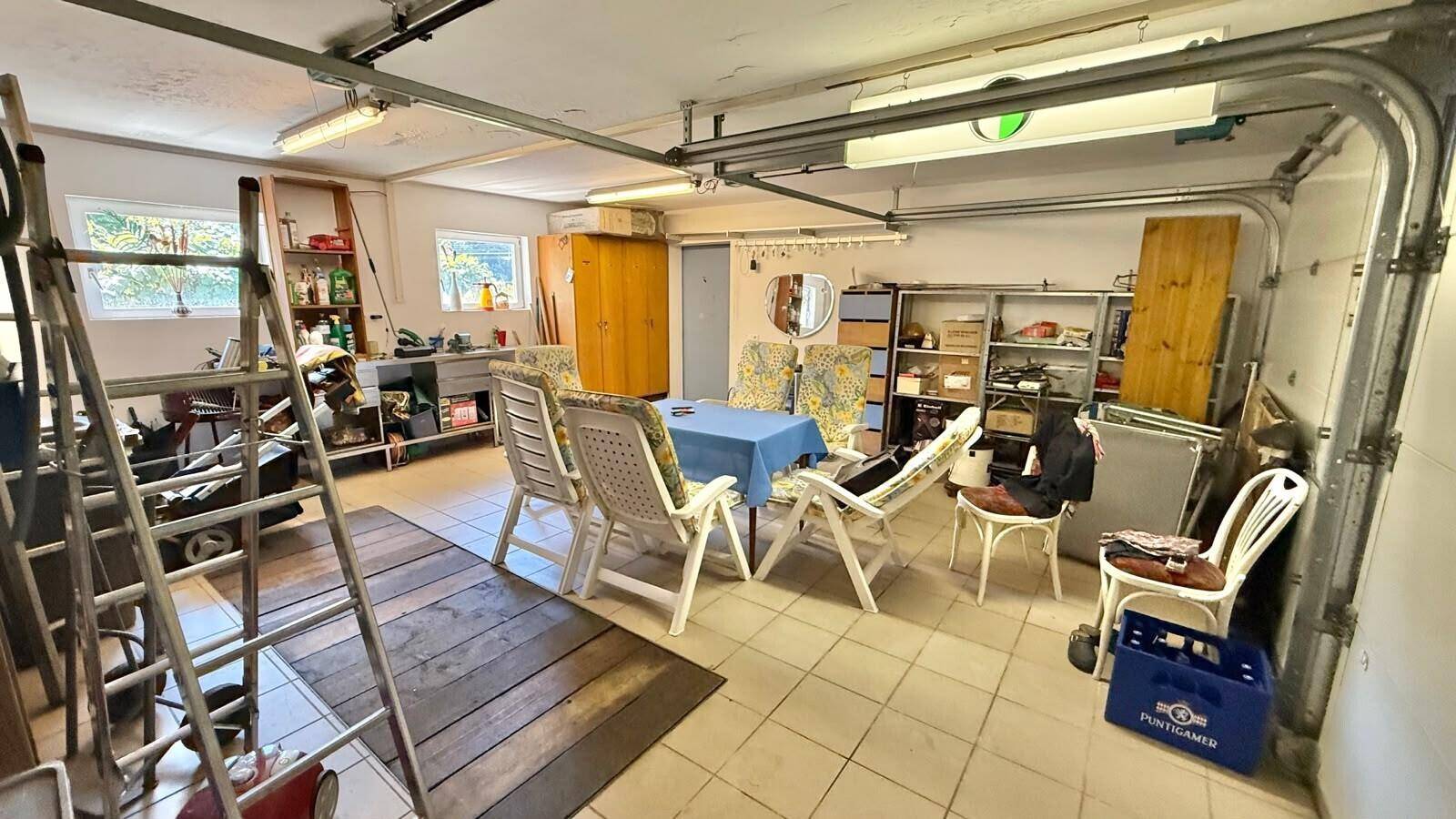 Geräumige Garage, die als Abstellraum und provisorischer Sitzbereich mit Fliesenboden genutzt wird.