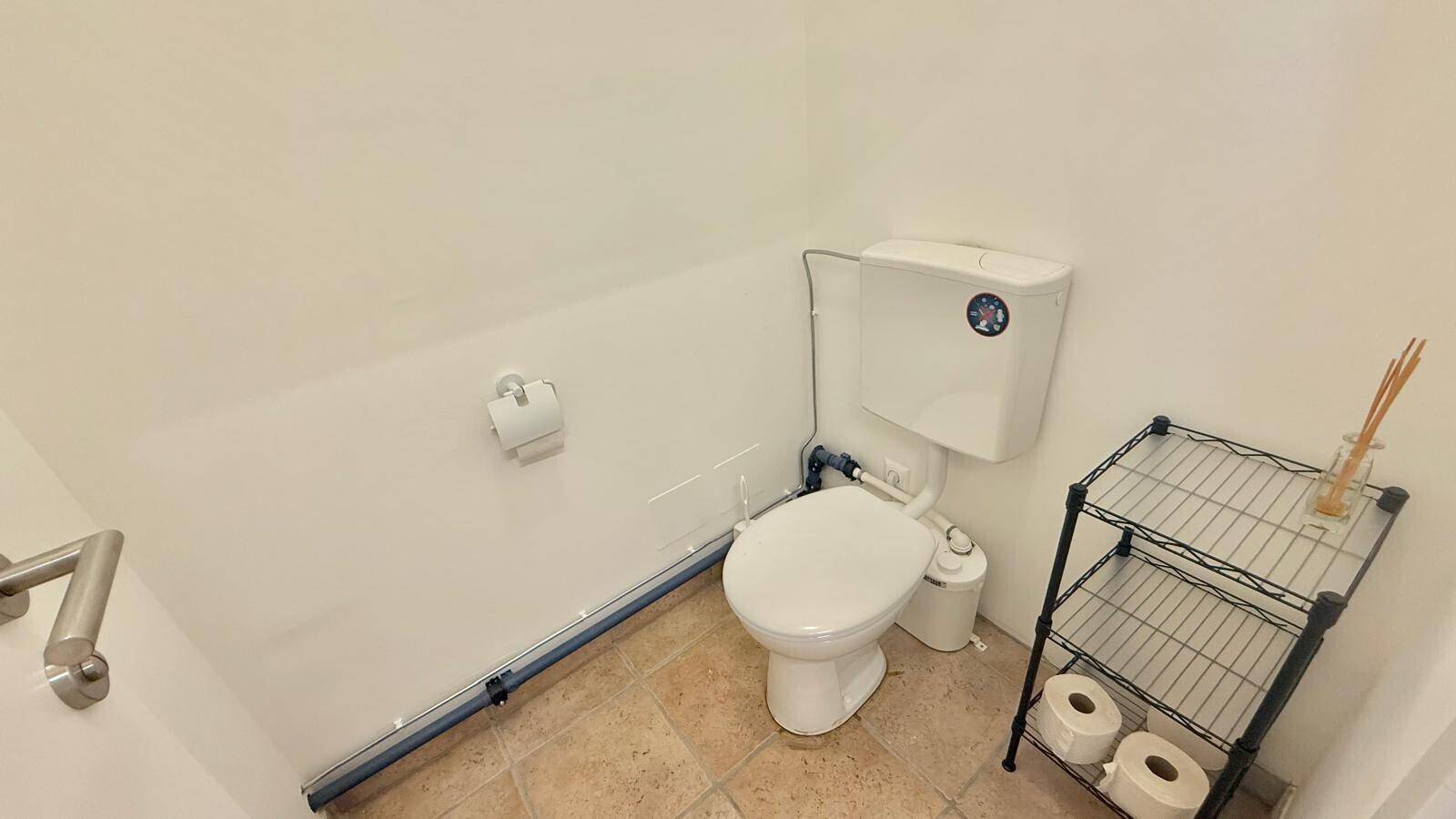 Einfache Gästetoilette mit WC, Fliesenboden und einem kleinen Regal, sauber und funktional.