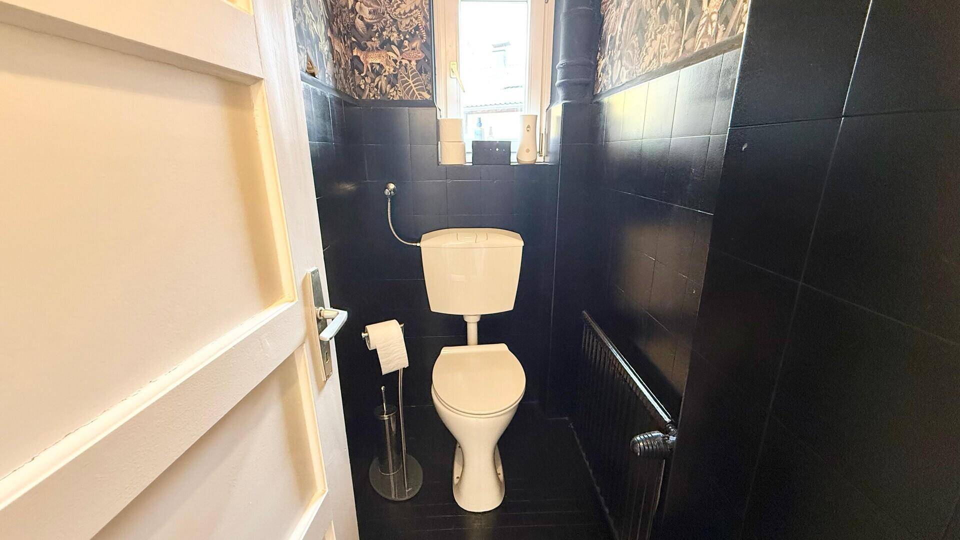 Kleines Gäste-WC mit dunklen Fliesen, Fenster und auffälliger Tapete.