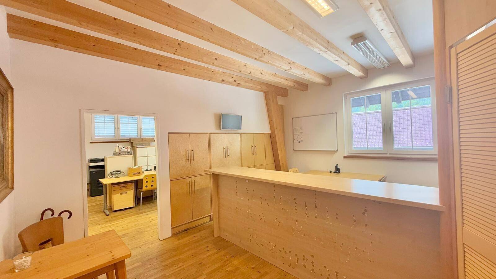 Geräumiger Bürobereich mit Holzbalken, großen Fenstern und integrierten Holzschränken, bietet viel Stauraum und Licht.