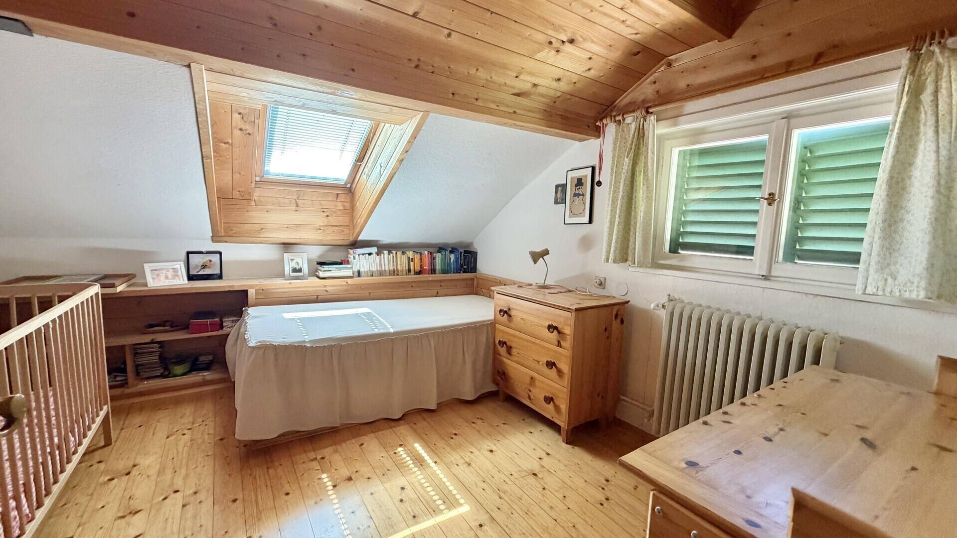 Helles Schlafzimmer im Dachgeschoss mit Holzdecke, Dachfenster und eingebauten Regalen.