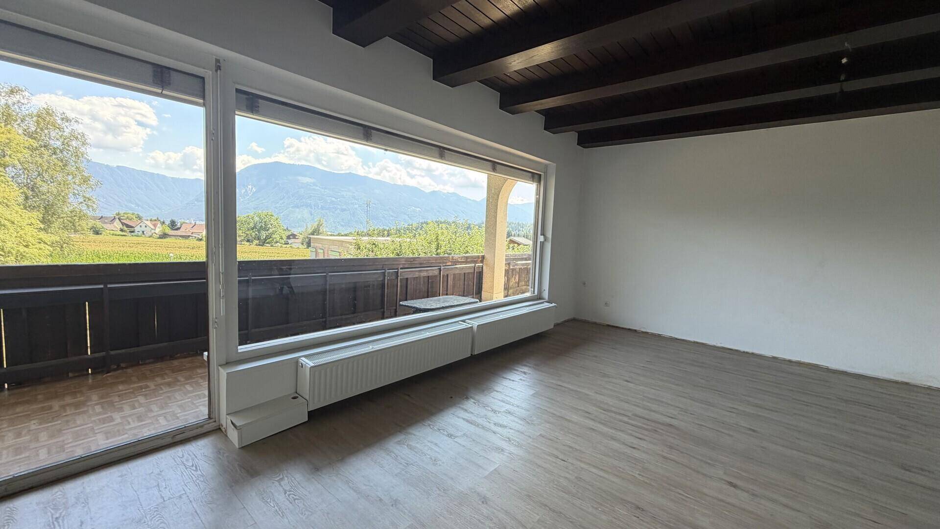 Heller Wohnraum mit Holzbalkendecke und Zugang zum Balkon mit Bergblick.